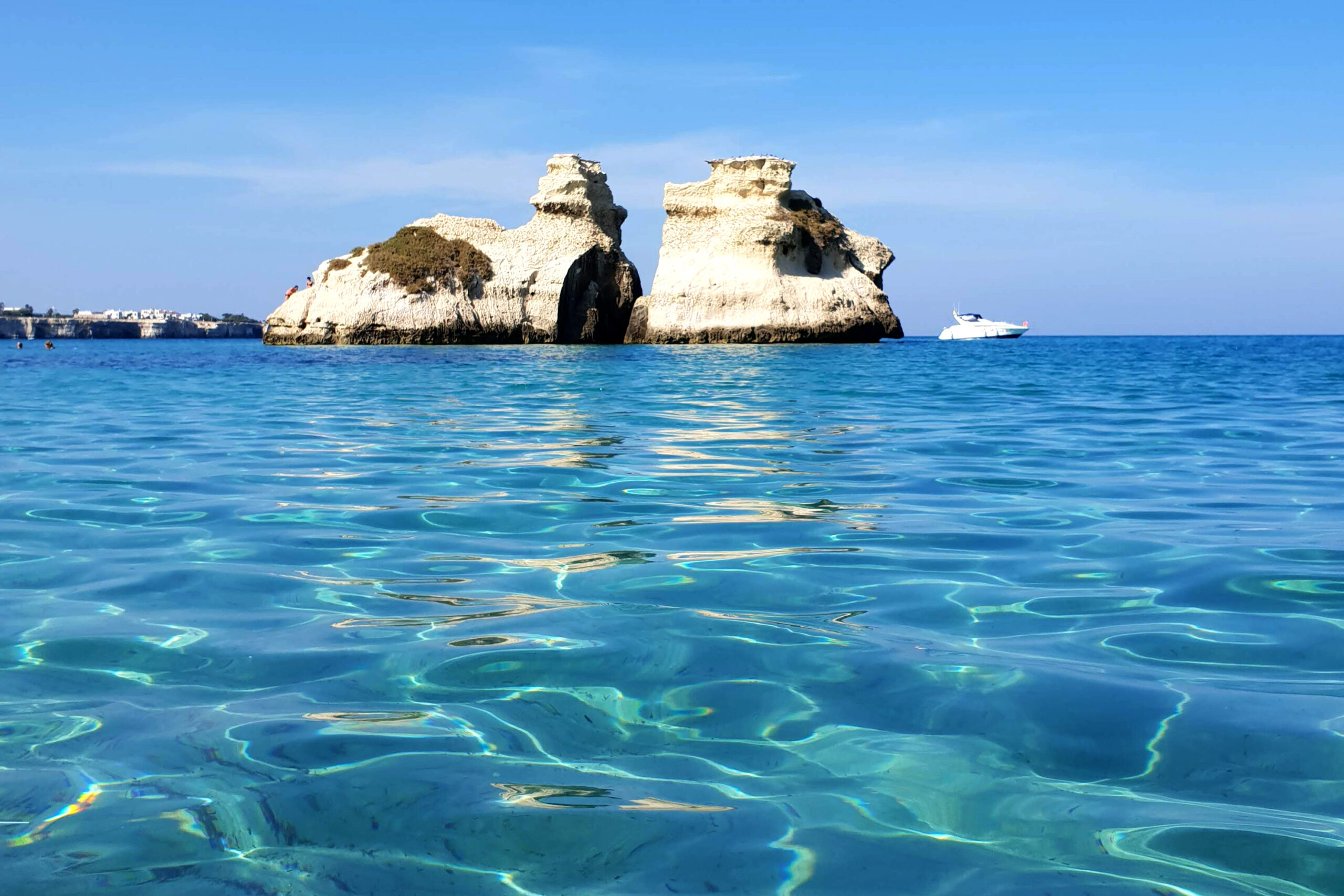 In foto si vede il mare blu del Salento e i due faraglioni chiamate le due sorelle