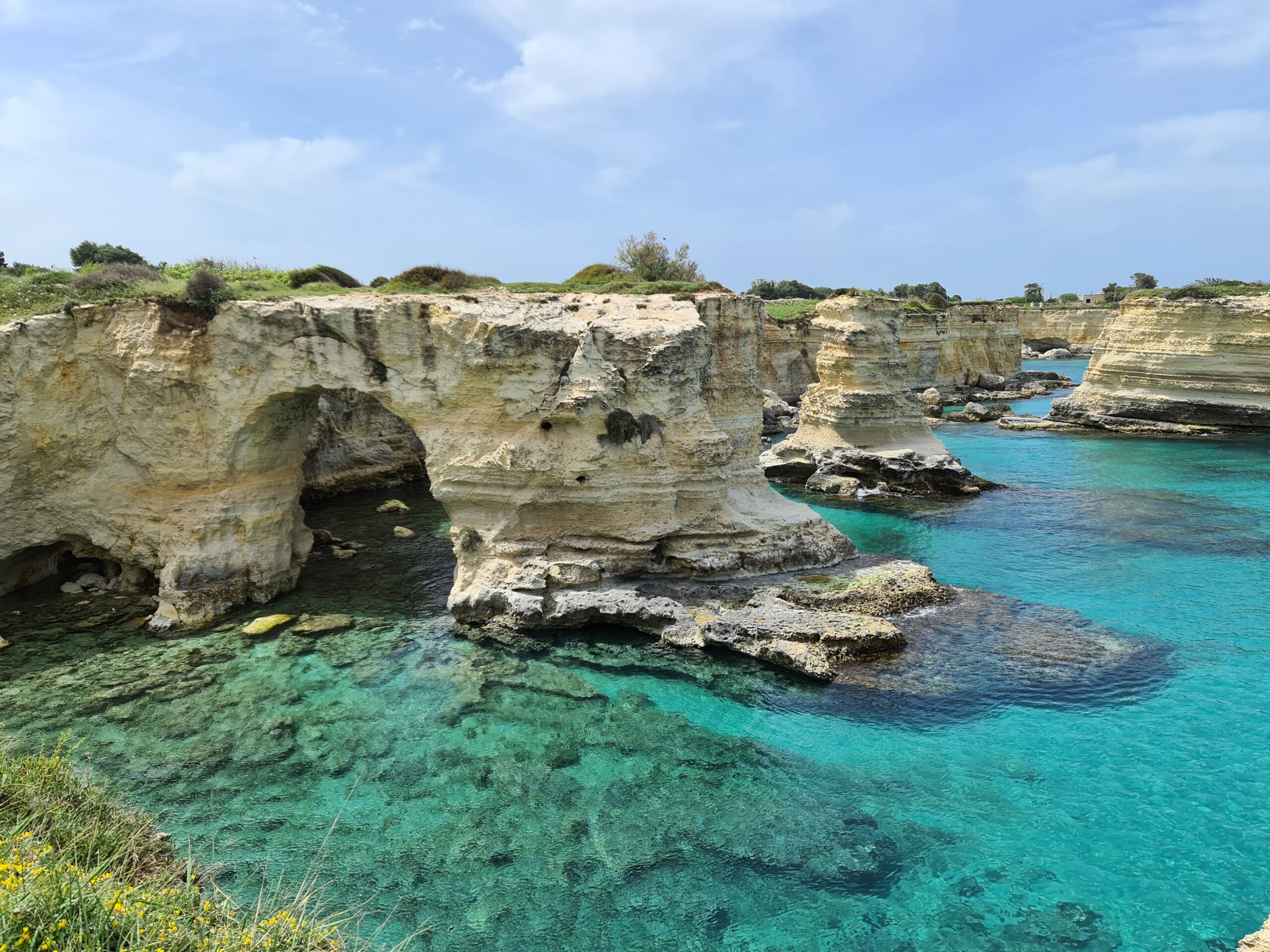 In foto si vedono i faraglioni di Sant'Andrea e l'arco naturale che si è formato nella roccia. Il mare è azzurro, calmo e limpido. 