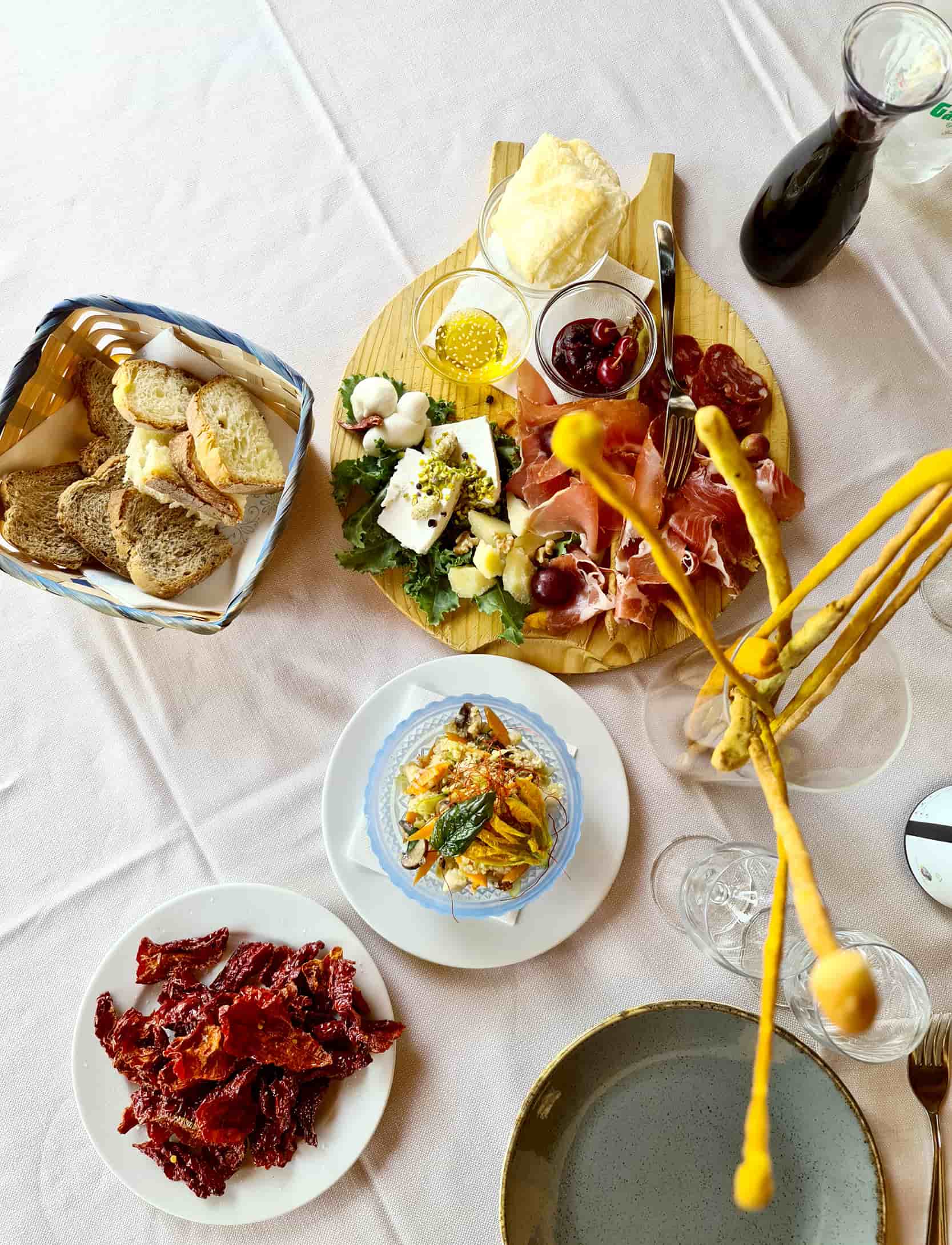 Una foto dall'alto alla tavola di masseria Lolivia, dove si vede un tagliere di salumi e formaggi, una caraffa di vino, i peperoni cruschi e dei grissini